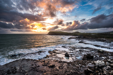 Colorful sunset over rock cliffs at Curio Bay, New Zealand. Big sea waves on the New Zealand shore coast line. Beautiful sky scenery.