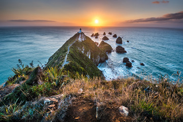 Sunrise at Nugget point Lighthouse. Magical colorful daybreak. Rays of sun light reflection. Wide angle panorama landscape photo.