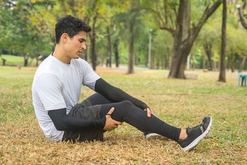 Young male athletes jogging in the park feel knee pain and sitting use hands hold on his knee.