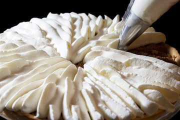 Piping chantilly cream onto a tart on a black background.