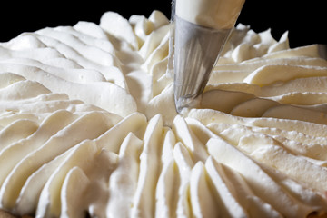 Piping chantilly cream onto a tart on a black background.