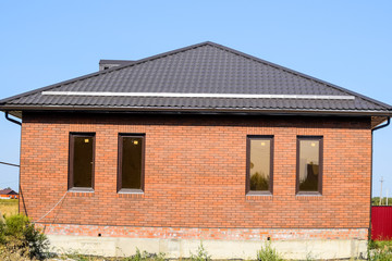 The house with plastic windows and a roof of corrugated sheet. Brown roof and brown brick