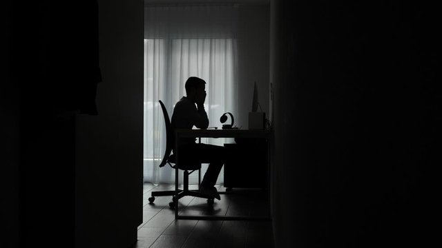Silhouette young man working on computer frustrated, tired and angry, rubs eyes. 