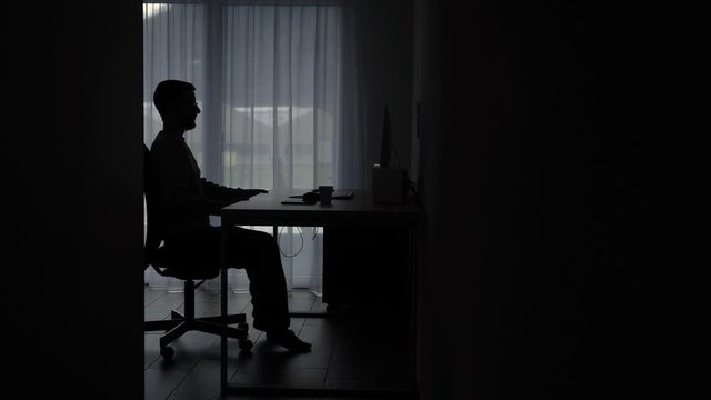 Entrepreneur working from home sits down at computer. Static shot.