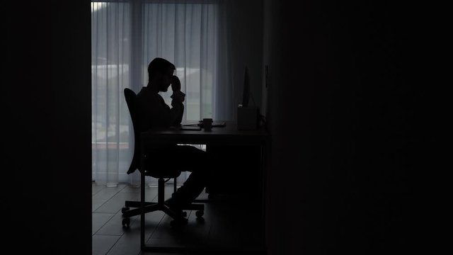 Silhouette of male on computer in dark room. Concept online crime and predator.