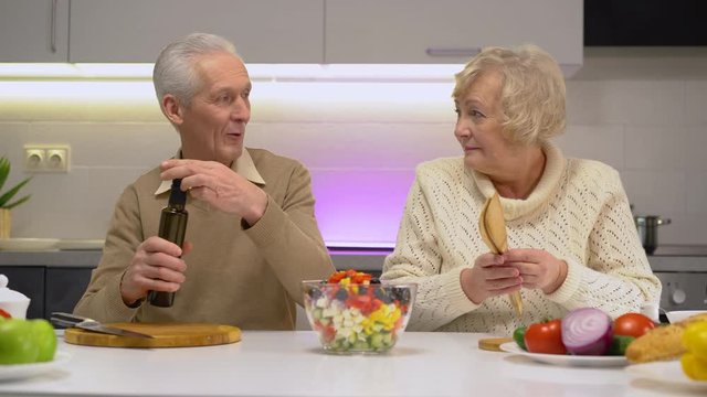 Elderly wife and husband cooking delicious vegetable salad, healthy life habits