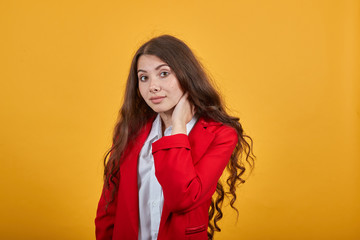 Brunette young woman in fashion white shirt and red jacket keeping hand on neck, having pain in muscules isolated on orange background in studio. People sincere emotions, lifestyle concept.