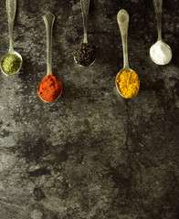 various spices and herbs on spoons on a dark background with free space for writing or recipes