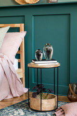 Stylish bedroom interior with design coffee table, plant, sculpture, shelf and elegant personal accessories. Beautiful bed sheets, blanket and pillow. Template. Modern home staging. Wall panelling.