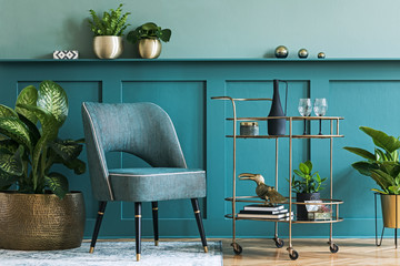 Interior design of luxury living room with stylish armchair, gold liquor cabinet, a lot of plants and elegant personal accessories. Green wall panelling with shelf. Modern home decor. Template. 