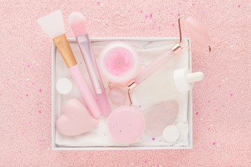 beauty box with rose quartz jade roller and stone, face serum and brush on pastel pink background