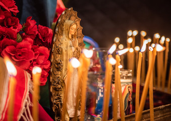 Small statue figures of the Virgin Mary and candles are lit at a church altar