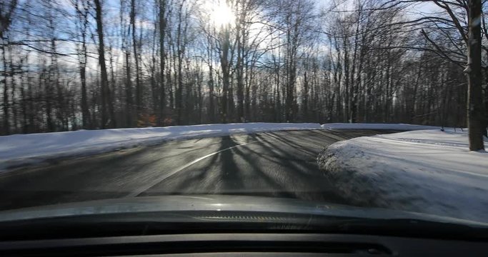 Driving on a scenic winter mountain road with snow and trees, beautiful sunny landscape, water drops on the windscreen with light flares