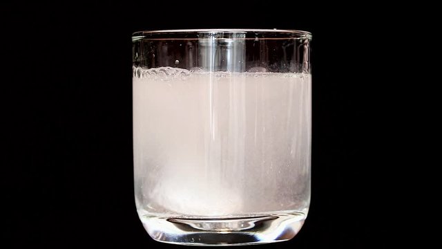 A white Tablet dissolve in rotating glass with water, on black background. Preparation of instant drink from soluble tablet.