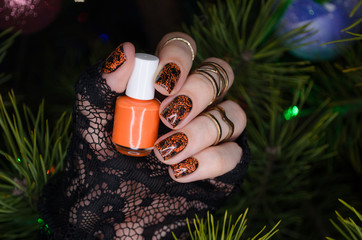 manicure nail art design for new year, black sparkling nails with orange nail art on the background of the Christmas tree