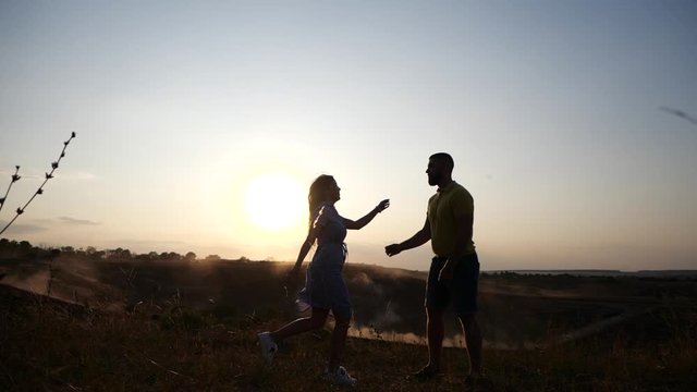 Young girl runs in slow motion toward a bearded young man and kisses him. Couple in rural landscape at breathtaking golden sunset.