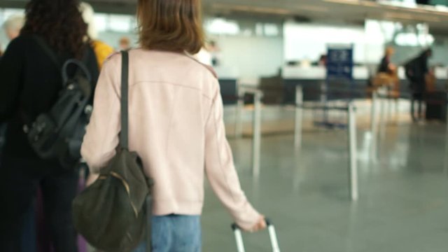 Brown-haired woman queues at the check-in desk at the airport. Travel concept