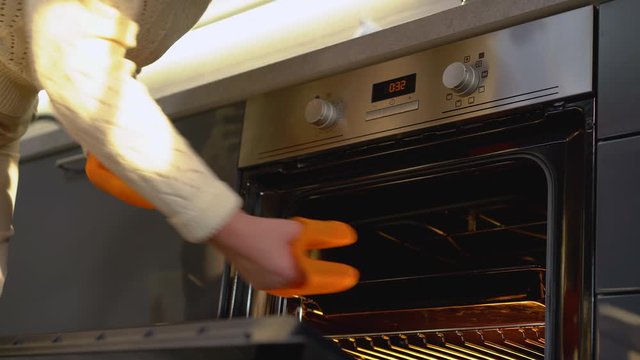 Lady taking hot baking pan from oven, using safe silicone mitts, cooking hobby