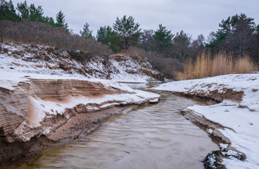 Tiny creek falls into Finnish Gulf though frozen sand dunes on Salmistu beach in Estonia. Empty...