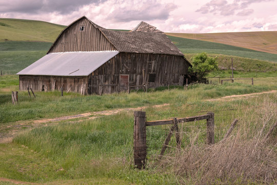 Old barn with a sunken roof, and a fence with barbed wire.  Image taken in the Palouse region of Washington state.