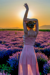 A young woman strolling through a lavender field at sunset, enjoying a beautiful moment in nature.