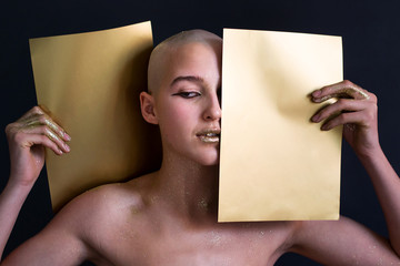photo young bald naked girl in gold spangles with two gold sheets in hands a dark background