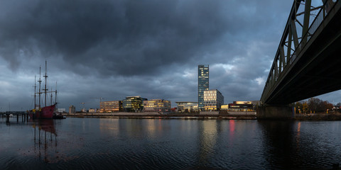 Überseestadt in Bremen, Germany with reflections on the river Weser and lights in the office buildings during blue houer with cloudy sky