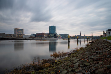 long exposure of the Überseestadt in Bremen, Germany with office buildings and cloudy sky and the river Weser in the foreground