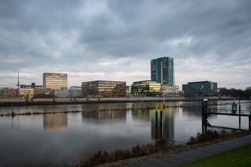 Fototapeta na wymiar Überseestadt in Bremen, Germany with reflections on the river Weser and lights in the office buildings during blue houer with cloudy sky