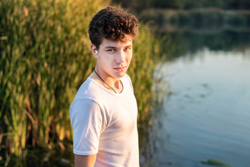 A teenage boy on a background of lakes and reeds, resting after a morning jog. The guy in the ear has a medical cotton wool because he has a sick ear