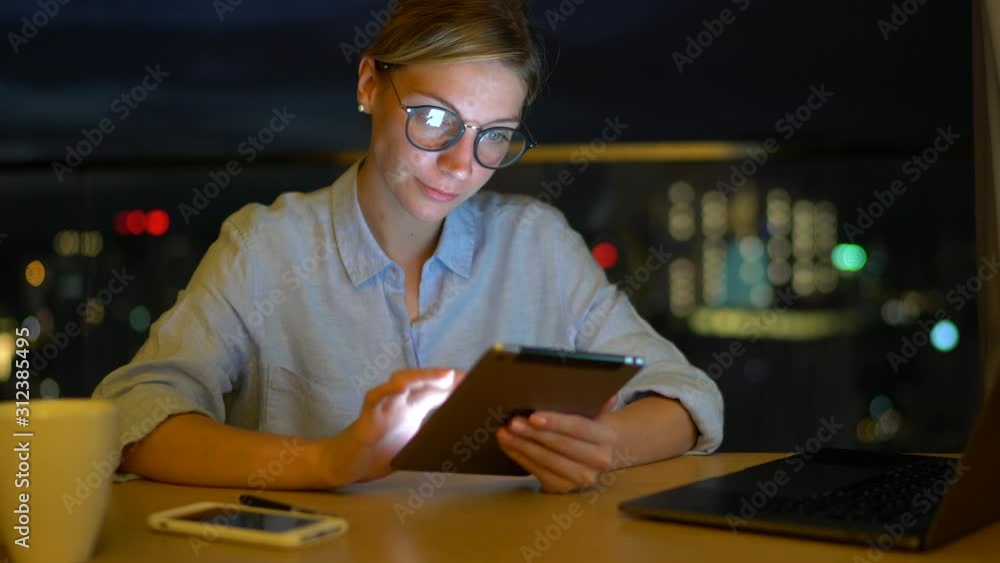 Poster young female blogger using digital gadget and laptop application during evening time for online netw