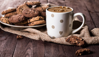 Cup of coffee and chocolate chip cookies on rustic wooden background.