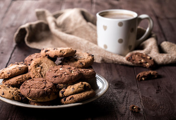 Cup of coffee and chocolate chip cookies on rustic wooden background.