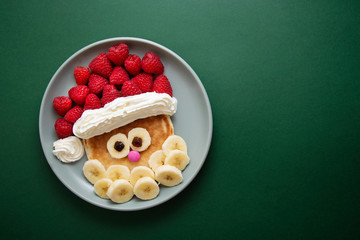 Winter food for kids. Christmas Santa pancake with raspberry and banana for children menu, green background, copy space.