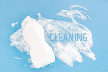 Bottle with washing agent with white soapy foam on a blue background. Cleaning/Washing concept....