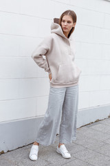 Beautiful young girl in fashionable biege hoodie and pants on light background. Walking on the...