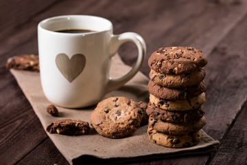 Cup of coffee with heart and chocolate chip cookies on rustic wooden background.