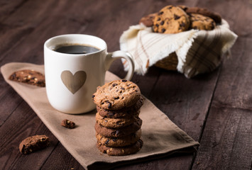 Cup of coffee with heart and chocolate chip cookies on rustic wooden background.