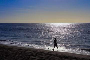 Silhouette of a woman walking on the beach at sunset