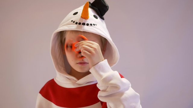 Funny blond child in nowman costume twists spiner on his nose. Portrait of boy on black background. 4K. Soothing toy. Autism. Exercise for Preschoolers