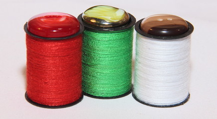 Three coils of red, green and white wire with buttons on top. Sewing accessories on a white background.