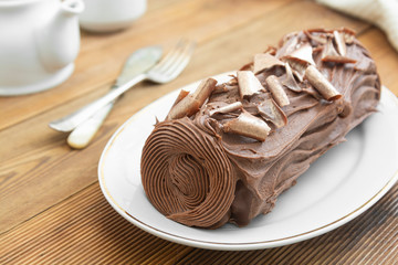 Chocolate swiss roll isolated on a wooden background. Chocolate sweet dessert. Pastry for breakfast or tea.
