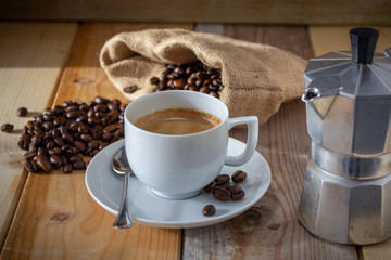 coffee in ceramic cup, moka coffee machine, coffee beans and burlap sack on wooden background