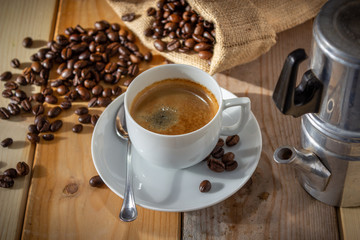 coffee in ceramic cup, neapolitan coffee machine, coffee beans and burlap sack on wooden background