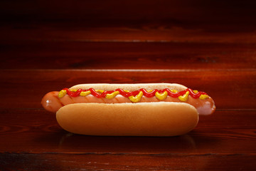 Classic hot dog with ketchup and mustard on a background of wooden boards.