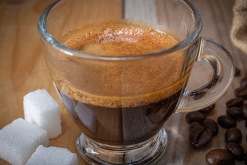 coffee in glass cup, sugar cubes, coffee beans and burlap sack on wooden background