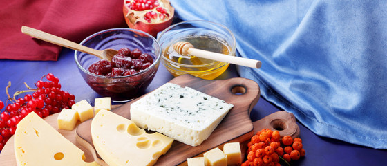 Cheese platter: variety of cheeses on wooden plate with fruits. Different types of cheese and honey. Hard cheese and berries on a classic blue background. Top view