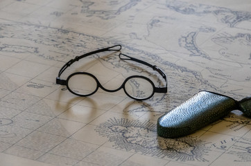 Pair of round magnifying spectacles on top of old sea faring map - obrazy, fototapety, plakaty