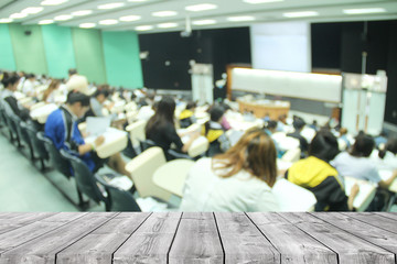 Wooden table in front of abstract blur background of student during study or quiz, test and exams from teacher or in large lecture room / University classroom.