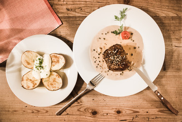 Delicious medium rare tenderloin veal steak with pepper sauce and baked potatoes with sour cream in rustic restaurant vintage table top view